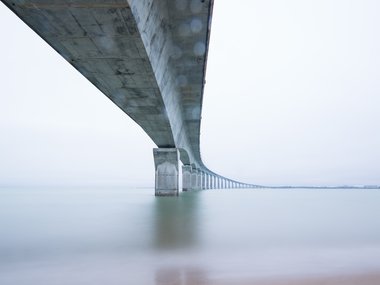 Der Blick unter eine Brücke mit vielen Betonpfosten als Träger im Meer.
