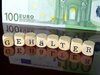 Buchstabenwürfel ergeben das Wort: Gehälter, welches sich auf einer roten, glatten Oberfläche wiederspiegelt und im Hintergrund ist ein 100 Euroschein..