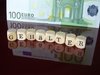 Buchstabenwürfel ergeben das Wort: Gehälter, welches sich auf einer roten, glatten Oberfläche wiederspiegelt und im Hintergrund ist ein 100 Euroschein..