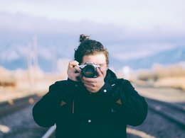 Ein Fotograf mit dunkler Jacke hält sich eine Canonkamera vor das Gesicht.