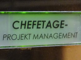 Eine Klingel mit leicht grünem Hintergrund und den Worten Chefetage, Projekt Management.