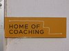 Ein gelbes Schild an einer Wand mit den Worten: Home of Coaching.