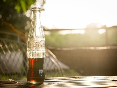 Das Bild zeigt eine  in der Sonne leuchtende Coca-Cola-Flasche. Coca-Cola ist die bekannteste Marke der Welt.
