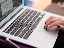 Eine Computertastatur mit einer Hand mit schwarzen Fingernägeln.