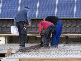Drei Männer in Arbeitskleidung arbeitet an einem Flachdach mit einer Solaranlage im Hintergrund.
