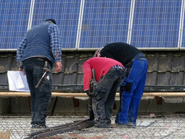 Drei Männer in Arbeitskleidung arbeitet an einem Flachdach mit einer Solaranlage im Hintergrund.