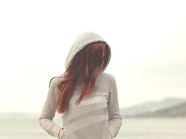 Eine Frau mit hellem Kapuzenpulli versteckt ihr Gesicht hinter ihren roten Haaren.