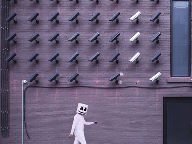 Zahlreiche Überwachungskameras zeigen auf eine weiß verkleidete Person.