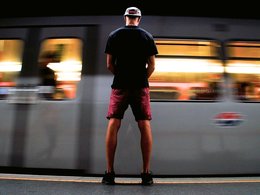 Ein Mann steht mit gesenktem Kopf neben einer vorbeifahrenden U-Bahn.