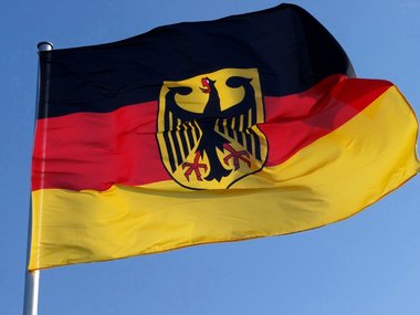 Eine wehende Deutschlandflagge mit Bundesadler vor blauem Himmel.