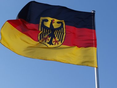 Eine wehende Deutschlandflagge mit Bundesadler vor blauem Himmel.