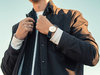 Das Bild zeigt einen Mann im Dresscode "Business-Casual" mit weißem Sweatshirt, dunkler Strickjacke, schwarzem Mantel und Uhr.