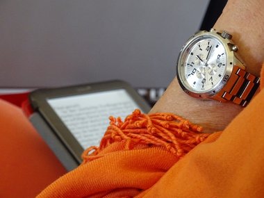 Zu sehen ist ein E-Book, eine Uhr und ein orangener Schal.