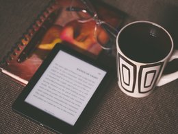Ein E-Book, ein Heft mit Brille und eine Tasse.