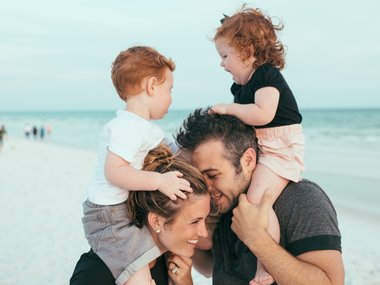 Eltern mit zwei Kindern auf den Schultern am Strand. Vereinbarkeit von Beruf und Familie