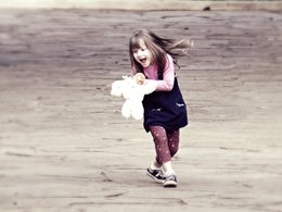 Elternzeit: Ein lachendes Mädchen spielt mit ihrem weißen Teddy.