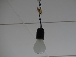 Eine nackte Glühbirne mit schwarzer Fassung hängt von der Zimmerdecke.