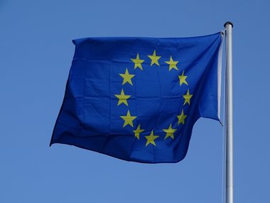 Blaue-Karte der EU: Fahne der Europäischen Union flattert vor blauem Himmel im Wind.