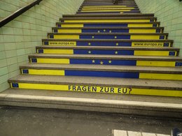 Eine Treppe mit den Farben der EU, gelb und blau, und einer Internetadresse und der Frage: Fragen zur EU?