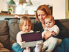 Das Bild zeigt eine Mutter mit ihren beiden Kindern auf dem Sofa, die auf ein Tablet schauen.