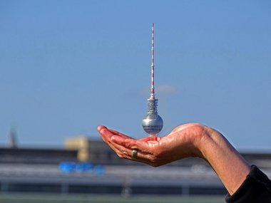 Der Berliner Fernsehturm in einer Hand vor blauem Himmel.