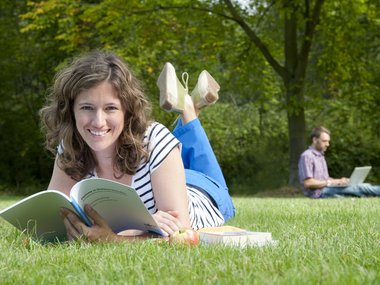 Fernstudium: Eine junge Studentin freut sich beim Lernen auf der Wiese im Sommer.