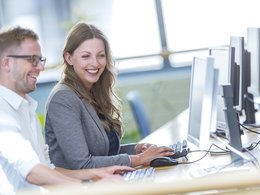 Eine Studentin und ein Student sitzen am Computermonitor und haben Spaß am Lernen.