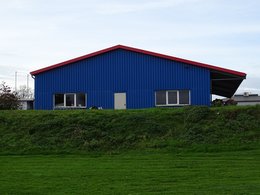 Das blaues Lagergebäude einer Firma vor einer Grünfläche mit einem Wall.