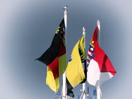 Drei Bundeslandflaggen hängen vor grauem Himmel herab - unter anderem die vom Bundesland Thüringen.