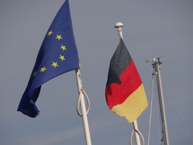 Die deutsche und die europäische Flagge vor blauem Himmel.