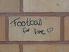 Rote Ziegelsteinmauer in einer Turnhallenkabine auf dem die Wörter Football for live geschrieben stehen.