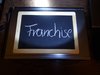 Auf einer Schiefertafel steht mit Kreide das Wort Franchise geschrieben.