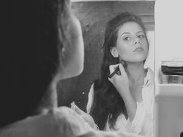 Schminken: Eine Frau mit langen Haaren pudert ihr Gesicht in einem Spiegel.