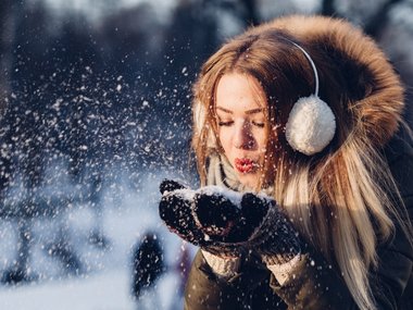 Glücksatlas-Lebenszufriedenheit: Eine junge Frau pustet Schnee von ihren Händen und strahlt dabei vor Freude und Glück.