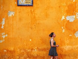 Eine Frau geht an einer orangenen Wand mit einem spanischen Straßenschild entlang.