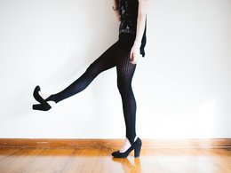 Die Beine einer Frau mit schwarzer Leggins und hochhackigen Schuhen, die ein Bein lustig in die Luft hebt.