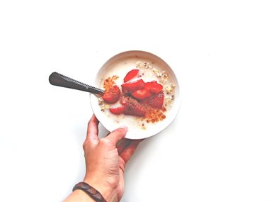 Eine Hand hält eine Schale mit Müsli und Erdbeeren.