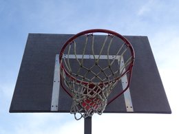 Ein Baskettballkorb mit Schild dahinter vor hellem Himmel.