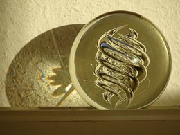 Eine Glaskugel spiegelt sich mit ihrem kunstvollen, spiralförmigen Inneren in der Sonne.