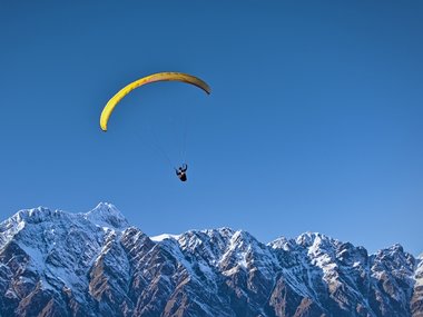 Ein Gleitschirmflieger am blauem Himmel über verschneiten Bergspitze.
