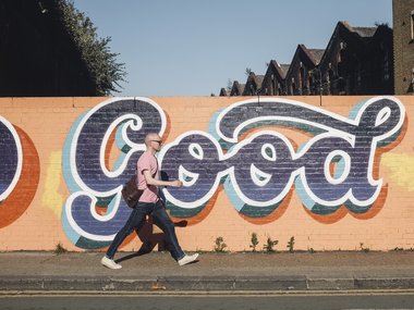 Ein Mann geht mit großen Schritten an einem Graffiti mit dem Inhalt: Good vorbei.
