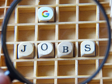 Stellenbörse: Eine Lupe vergrößert das Logo von Google und das Wort JOBS.