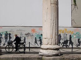 Eine Wand mit Graffitischmiererei mit einem Mann auf seinem Fahrrad und einer großen Säule.