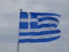 Die griechische Flagge weht vor grau-blauem Himmel.