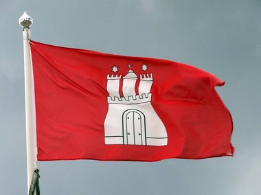 Die rote Flagge von Hamburg mit der weißen Burg weht an einem Fahnenmast im Wind.