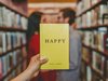 Ein gelbes Buch mit der Aufschrift: happy wird vor ein sich anschauendes Paar gehalten.