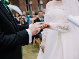 Ein Mann steckt einer Frau, beide in Hochzeitskleidung, einen Ring an.