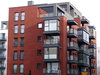 Das Bild zeigt die schwarzen Fenster und Balkone zahlreicher Wohnungen von einem roten Haus.