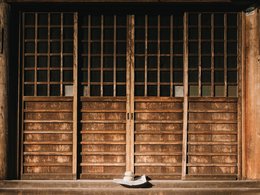 Eine japanische Holztür mit zwei kleinen, runden Steinen und einem Zettel davor.