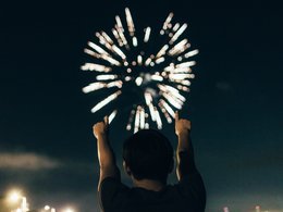 Ein junger Mann jubelt mit erhobenen Händen einem Feuerwerk zu.